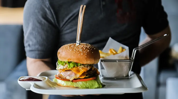 man-holding-plate-with-beef-burger-lettuce-cheese-tomato-cucumber-egg-french-fries-sauce-side-view.jpg